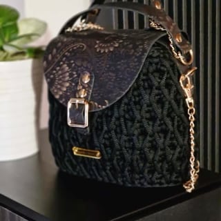 Black quilted handbag with ornate leather flap, metal buckle, and gold chain strap