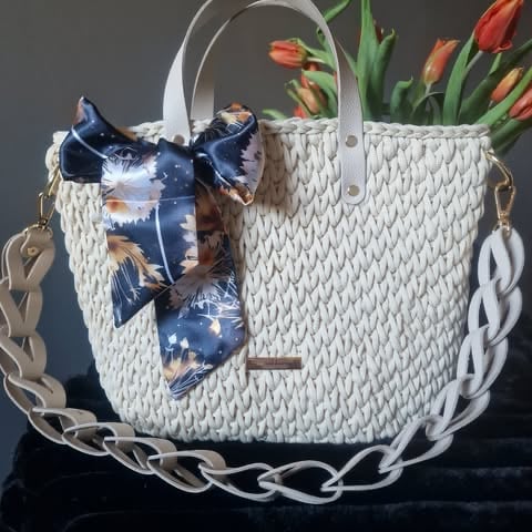 White woven handbag with blue floral scarf bow, chain handles, and red tulips in the background