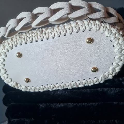 White leather clutch with braided trim and gold studs sitting on black fabric