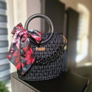 Black woven handbag with metal handles and a red floral patterned silk scarf bow