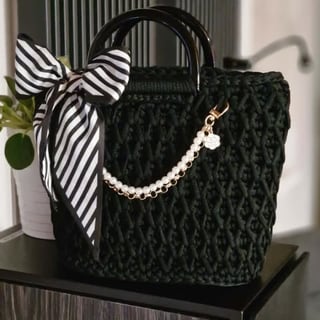Green knitted tote bag with black handles, white pearl chain strap, and black and white striped bow accent
