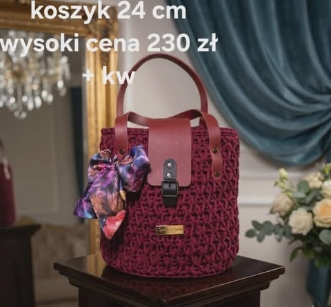 Burgundy patterned bucket handbag with handles and decorative scarf, displayed on black stand in elegant interior setting