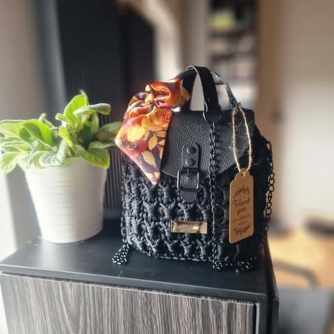 Black patterned handbag with colorful floral scarf on a dark table next to a potted plant