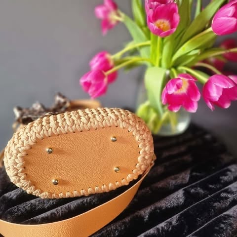 Handmade leather acorn-shaped ornament with decorative stitching on dark fabric, with pink tulips in background vase